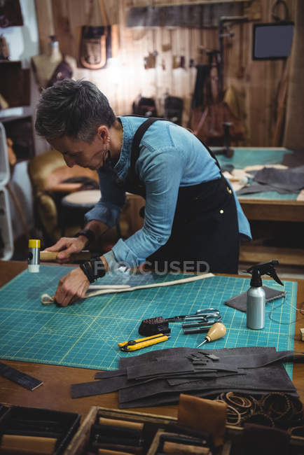 Mature craftswoman hammering leather in workshop — Stock Photo
