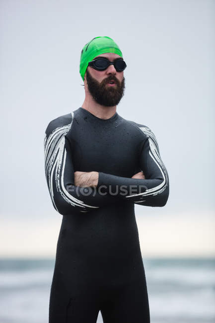 Спортсмен в мокром костюме стоит со скрещенными руками на пляже — стоковое фото