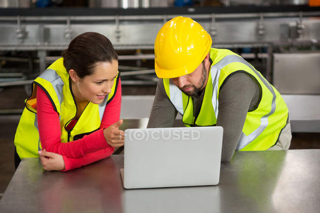 Trabalhadores masculinos e femininos usando laptop na fábrica — Fotografia de Stock