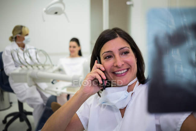 Dentiste vérifiant le rapport de rayons X tout en parlant sur téléphone portable à la clinique esthétique — Photo de stock
