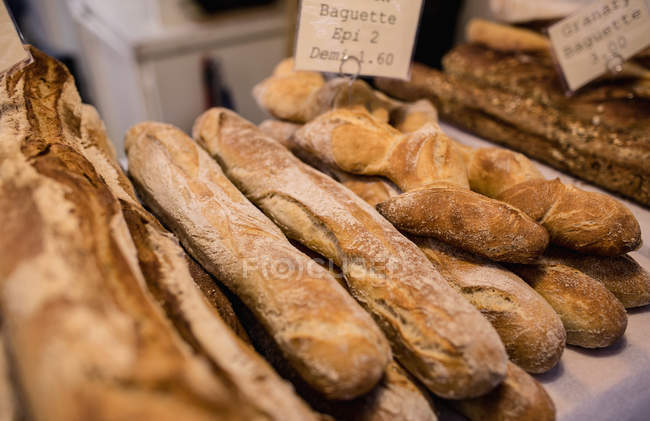 Varios tipos de pan apilados juntos en el mostrador de panadería en el supermercado - foto de stock