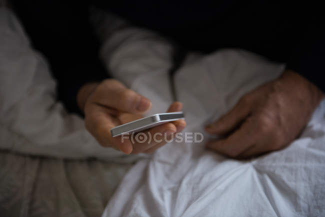 Середина людини, що використовує мобільний телефон на ліжку вдома — стокове фото