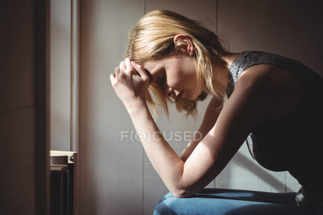Donna tesa seduta con mano sulla fronte a casa — Foto stock