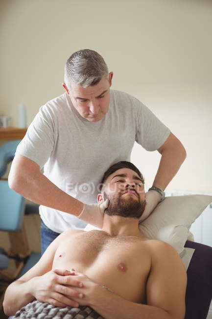 Физиотерапевт осматривает шею пациента-мужчины в клинике — стоковое фото