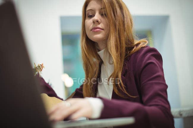 Рыжая женщина использует ноутбук во время еды салата — стоковое фото