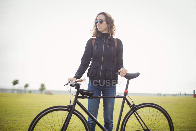 Жінка з сонцезахисними окулярами тримає велосипед у парку — стокове фото
