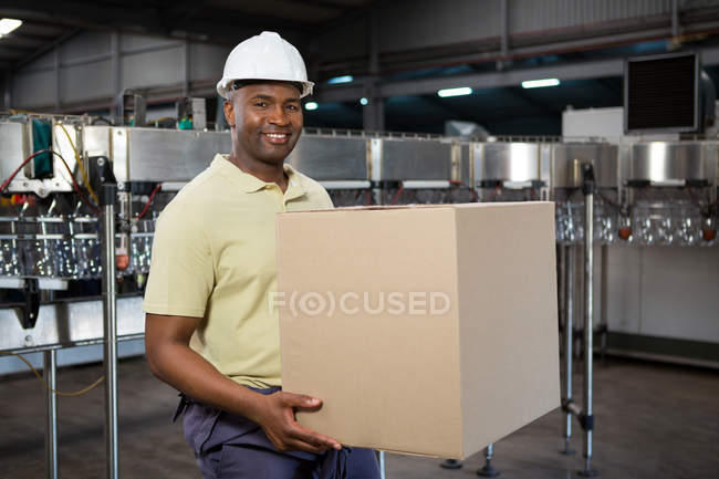 Retrato del empleado masculino sonriente que lleva la caja de cartón en la fábrica del jugo - foto de stock