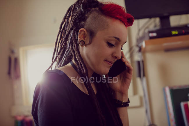 Женщина-парикмахер разговаривает по мобильному телефону в магазине дредов — стоковое фото