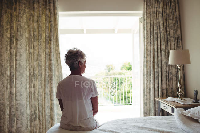 Femme âgée assise sur un lit dans la chambre à coucher à la maison — Photo de stock
