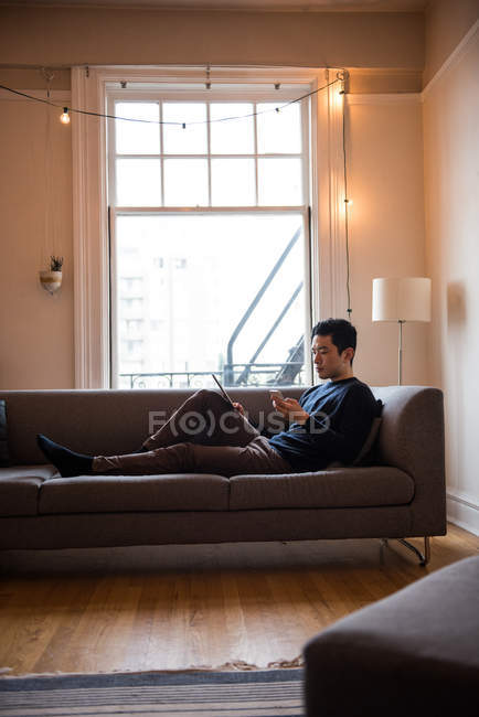 Homem usando tablet digital e telefone celular na sala de estar em casa — Fotografia de Stock