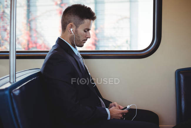 Empresário ouvindo música e usando no celular no trem — Fotografia de Stock