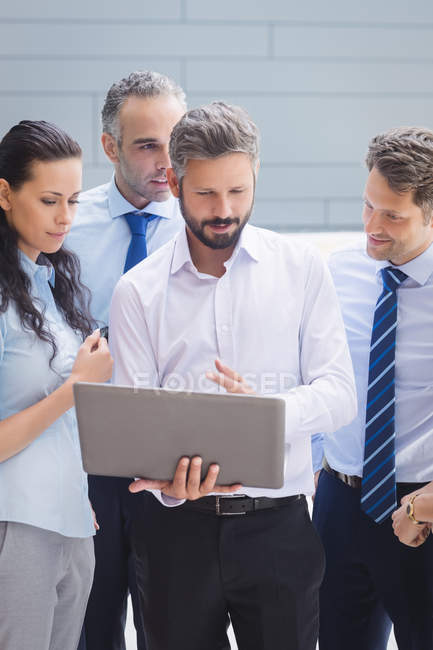 Group of business people discussing over laptop outside office building — Stock Photo