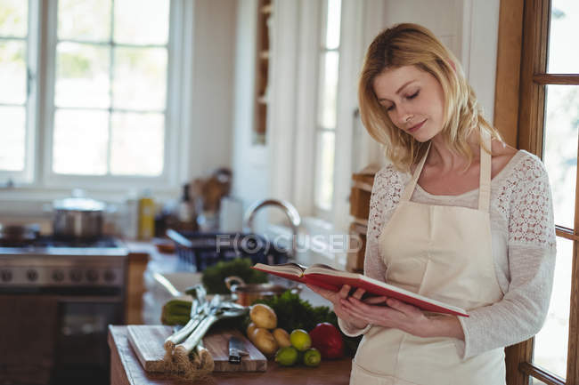 Bella donna che legge libro di ricette in cucina a casa — Foto stock