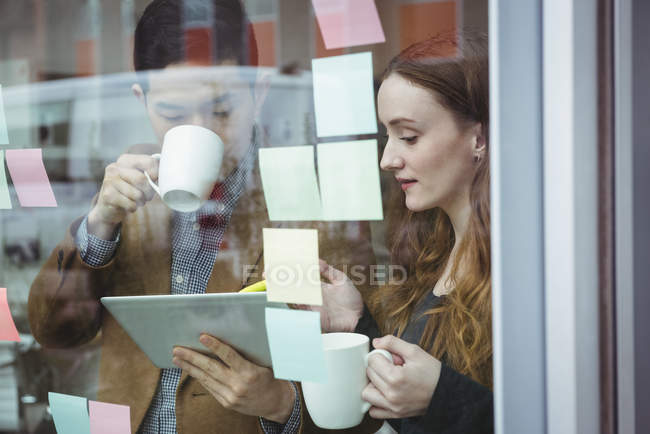 Executivos de negócios discutindo sobre tablet digital enquanto toma uma xícara de café no escritório — Fotografia de Stock