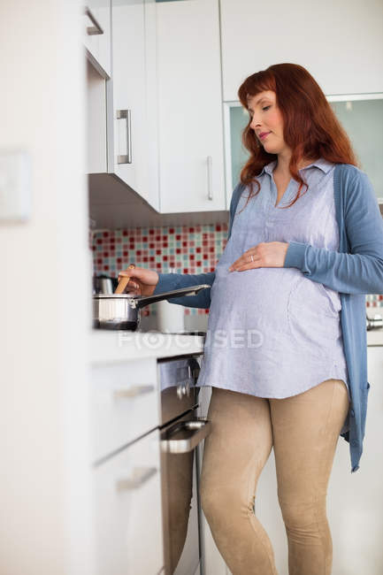 Беременная женщина готовит еду на кухне дома — стоковое фото
