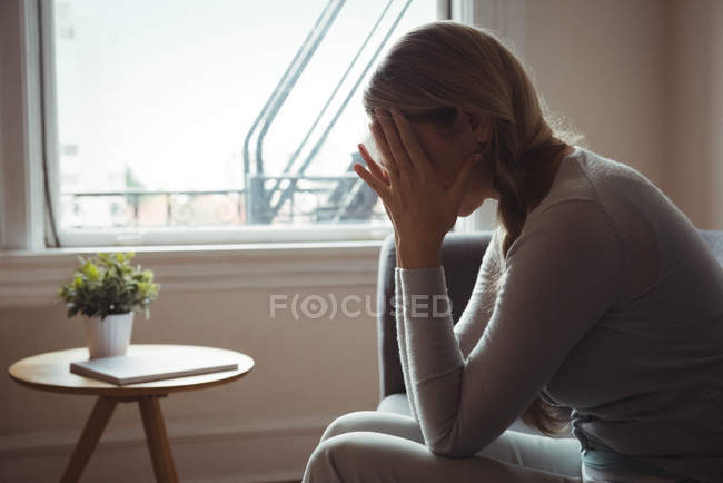 Напряженная женщина сидит на диване в гостиной на дому — стоковое фото
