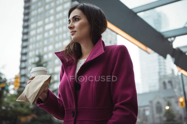 Businesswoman holding disposable coffee cup and parcel while walking on street — Stock Photo