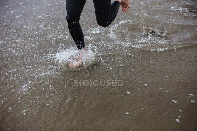 Bassa sezione di atleta in muta che corre sulla spiaggia — Foto stock