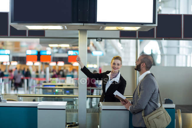 Asistente de facturación de la aerolínea que indica la dirección al viajero en el mostrador de facturación en la terminal del aeropuerto - foto de stock