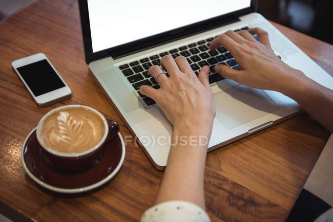 Las manos de la mujer de negocios utilizando el ordenador portátil en la mesa de café - foto de stock