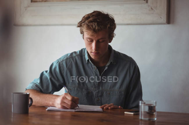 Mann sitzt am Schreibtisch und schreibt zu Hause an Notizbuch — Stockfoto