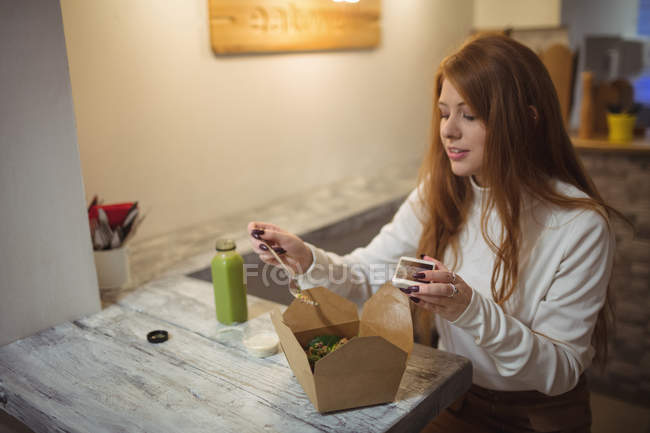 Woman holding mobile phone while eating in the restaurant — Stock Photo