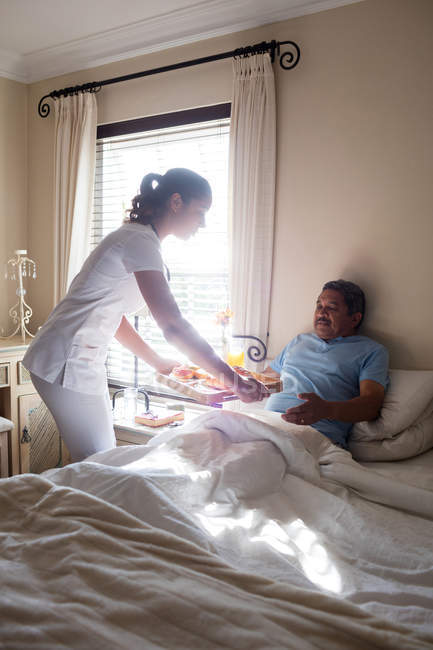 Лікар, що подає сніданок старшому пацієнту в спальні — стокове фото