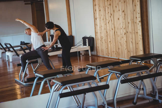 Coach helping woman while practicing pilates in fitness studio — Stock Photo
