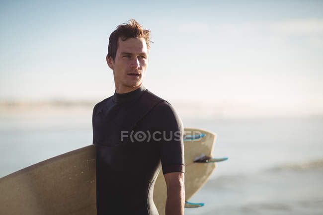 Surfista atencioso de pé com prancha na praia — Fotografia de Stock