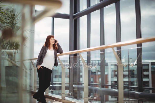 Grávida empresária falando no celular perto do corredor no escritório — Fotografia de Stock