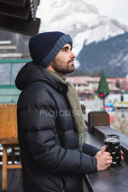 Homem em roupas de inverno segurando copo de cerveja no terraço ao ar livre — Fotografia de Stock