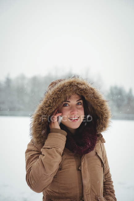 Улыбающаяся женщина в меховой куртке разговаривает по мобильному телефону зимой — стоковое фото