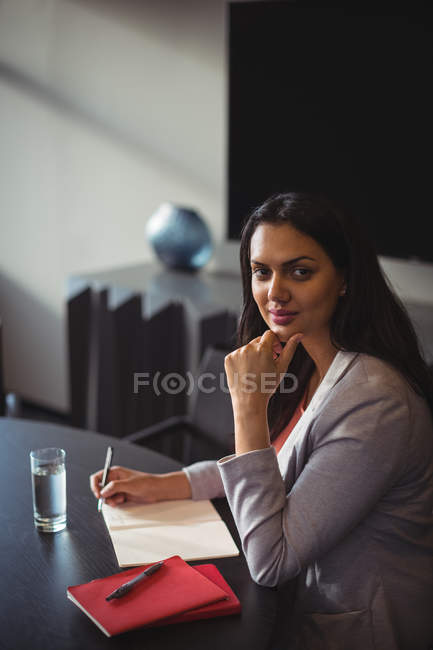 Portrait of businesswoman writing in diary in office — Stock Photo