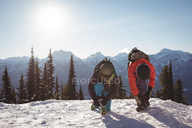 Two skiers tying shoelaces in snow covered mountains during winter — Stock Photo