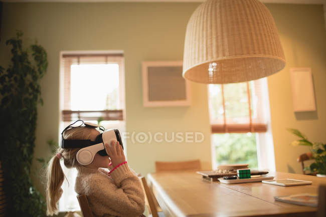 Дівчина сидить за столом і використовує віртуальну гарнітуру вдома — стокове фото