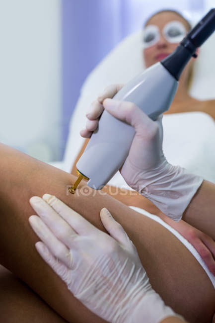 Paciente femenina que recibe tratamiento de depilación láser en pierna en salón de belleza - foto de stock