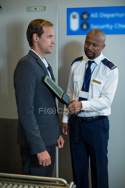 Oficial de seguridad del aeropuerto usando un detector de metales de mano para comprobar un viajero en el aeropuerto - foto de stock
