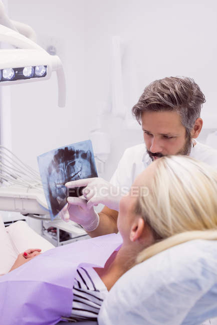Dentista mostrando radiografía a paciente en clínica - foto de stock
