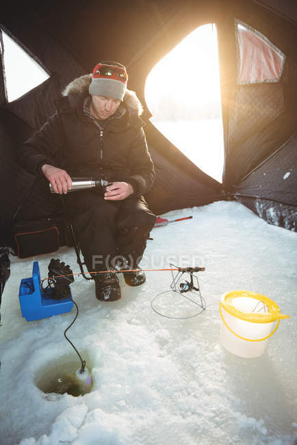 Взрослый ледяной рыбак наливает кофе в палатку — стоковое фото