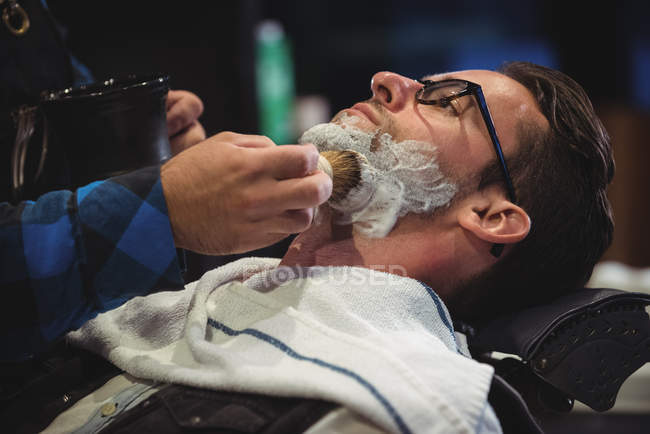 Seção média de barbeiro aplicando creme na barba do cliente na barbearia — Fotografia de Stock