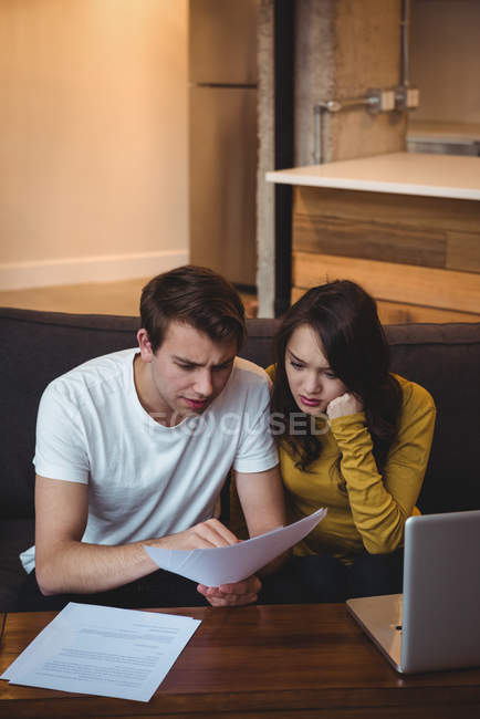 Пара, сидящая на диване и обсуждающая финансовые документы в гостиной дома — стоковое фото