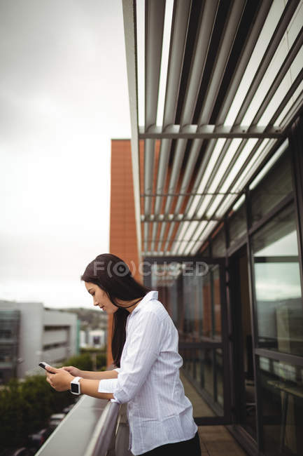 Vista lateral da empresária usando telefone celular na varanda do escritório — Fotografia de Stock