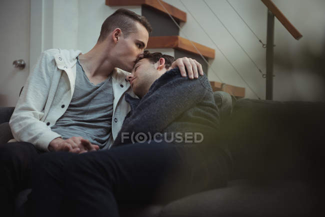 Gay pareja besándose y abrazando en sofá en casa - foto de stock