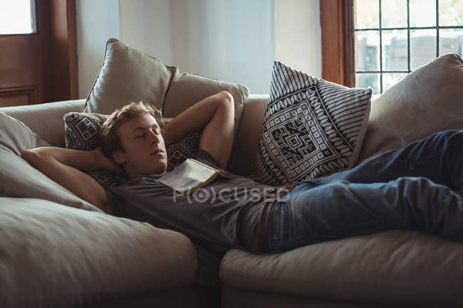 Hombre durmiendo en el sofá con un libro en el pecho en la sala de estar - foto de stock