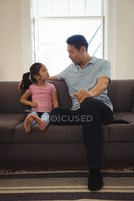 Отец и дочь взаимодействуют во время использования цифрового планшета в гостиной дома — стоковое фото