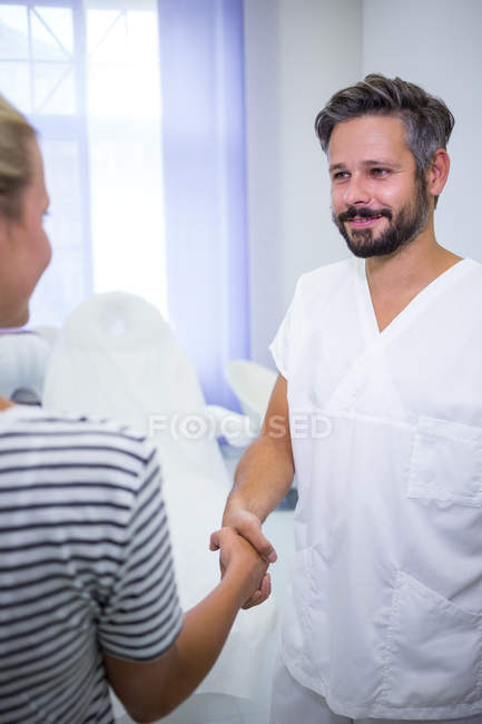 Médico estrechando la mano con paciente femenina en la clínica - foto de stock