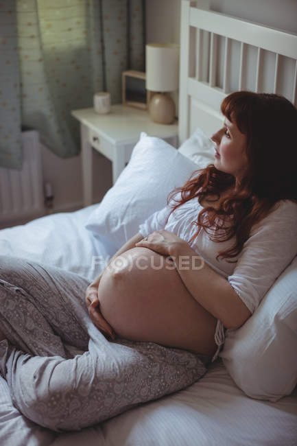 Thoughtful pregnant woman relaxing on bed in bedroom — Stock Photo