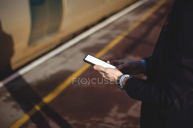 Vista recortada del hombre de negocios utilizando el teléfono móvil en la estación de tren - foto de stock