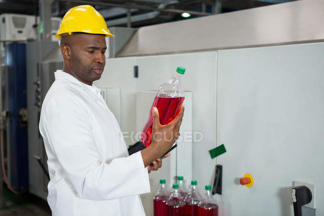 Серьезный рабочий осматривает бутылки на соковом заводе — стоковое фото