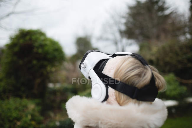 Mujer con abrigo de furia usando auriculares de realidad virtual al aire libre - foto de stock